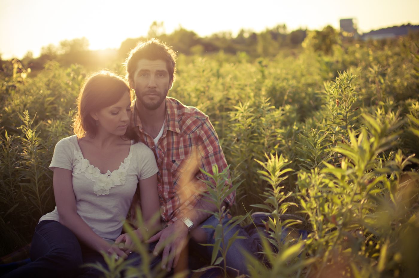 A couple sitting close together in tall grass at sunset
