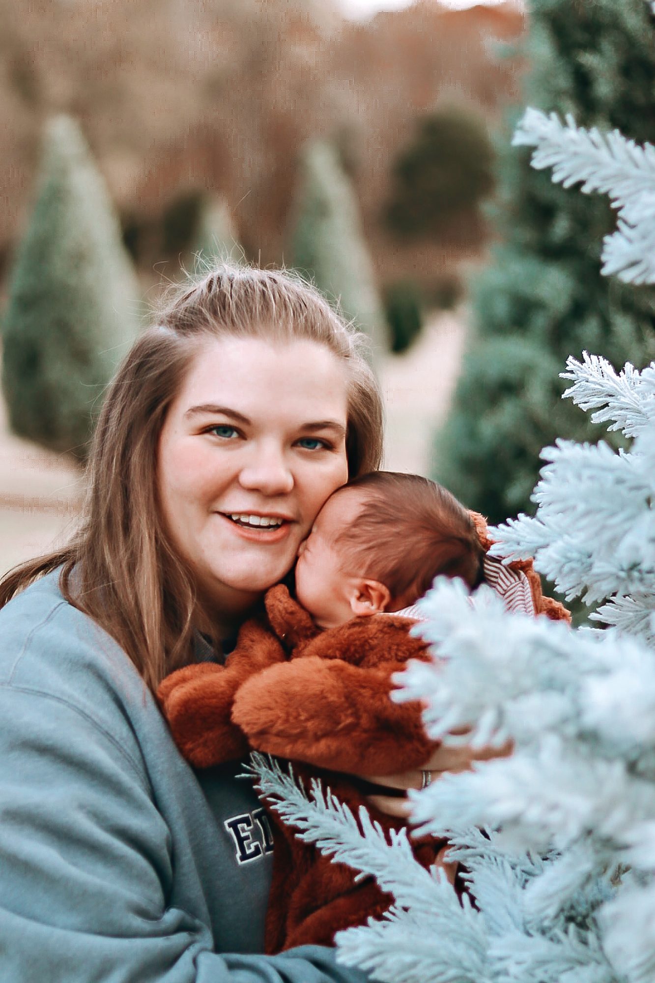 Mom snuggling her baby beside a frosted Christmas tree